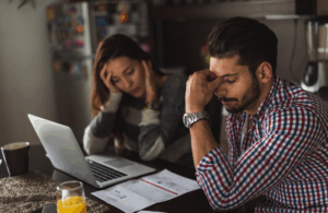 A frustrated couple at a kitchen table reviewing documents and bills, representing the real-life impact of criminal charges and policy shifts on Texas families.