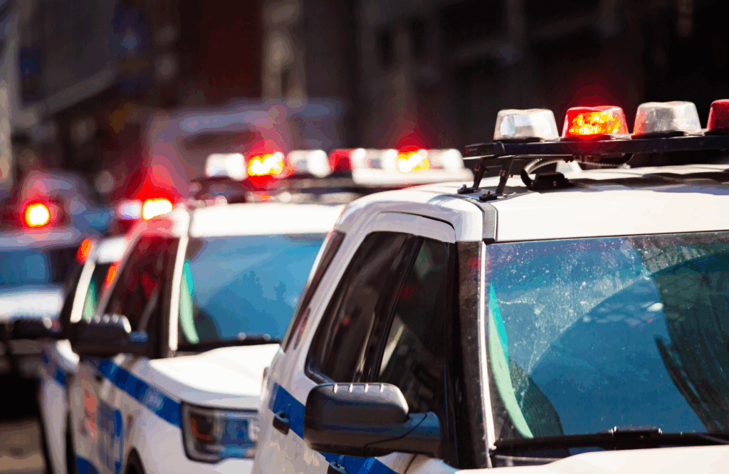 Line of police vehicles with flashing red and blue lights, representing expanded immigration enforcement through ICE-sheriff cooperation in Texas counties
